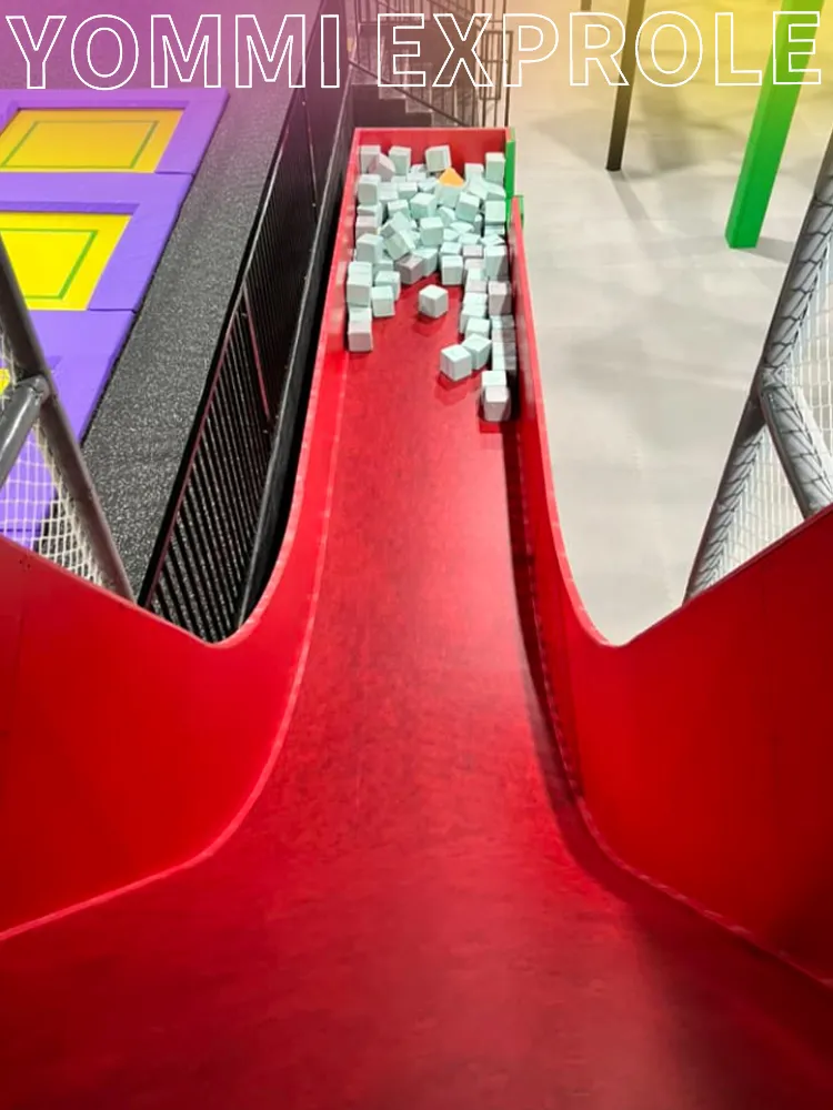 Multi-level red devil slide attraction designed by a source factory, maximizing the vertical space and ROI of an indoor trampoline park with high ceilings.