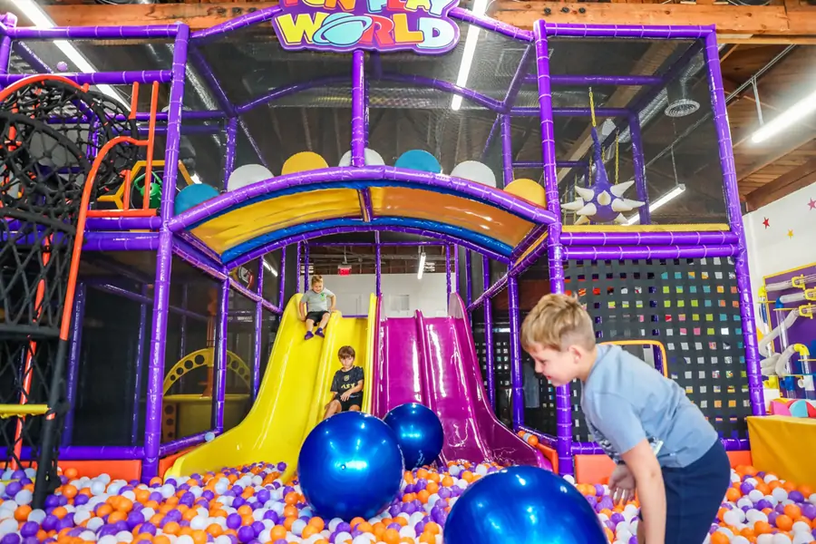 Multi-level custom indoor playground structure manufactured by Yommi featuring slides and a ball pit