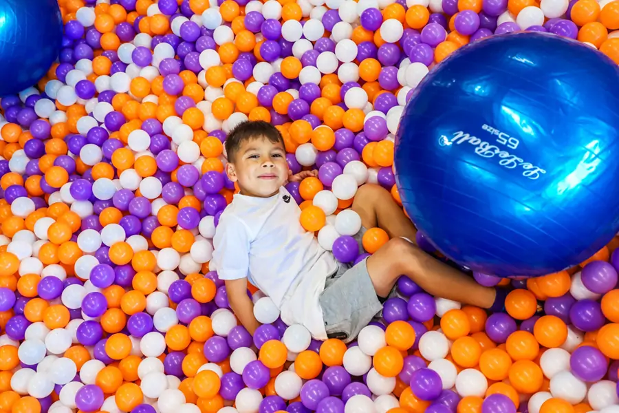 Happy boy relaxing in a giant ball pit with a large blue sensory yoga ball