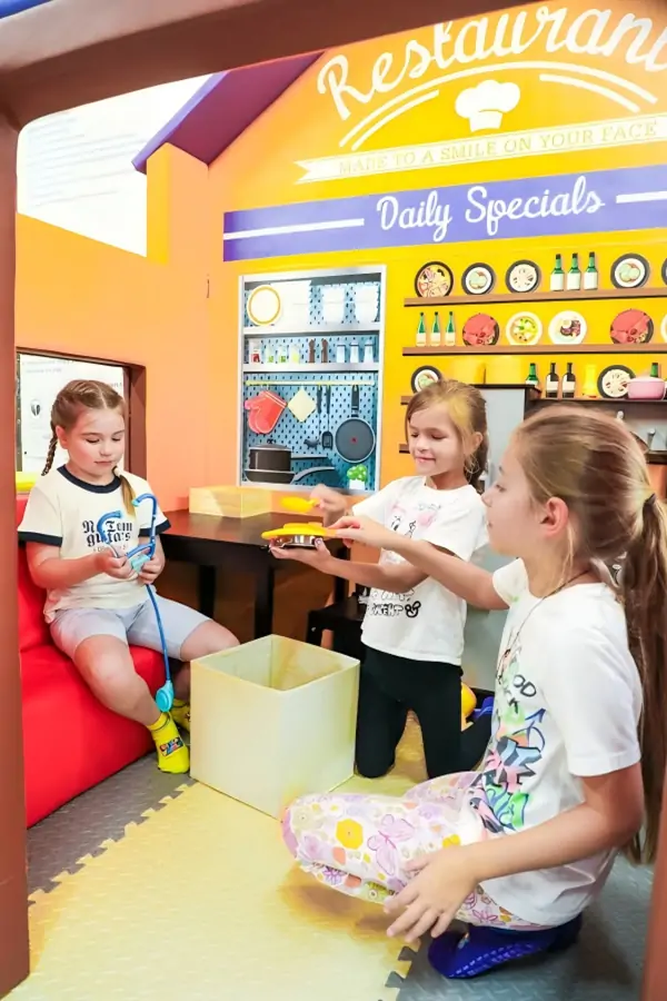 Three young girls playing together in a highly detailed pretend play restaurant house