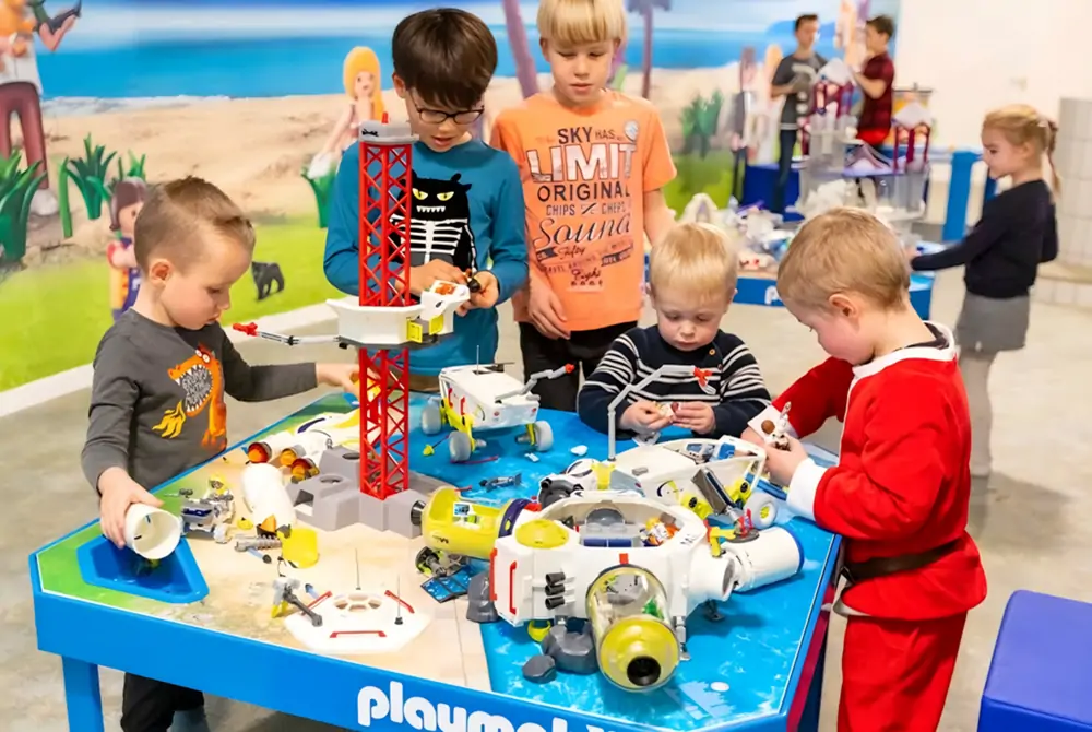 Young children playing with building blocks and toy vehicles at a blue building blocks activity table in Speelpunt Zwevegem indoor playground