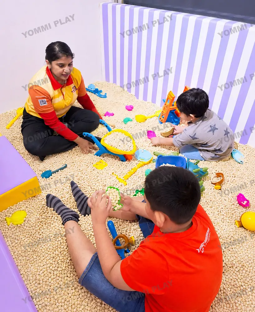 Hygienic eco-friendly cassia seed sand pit area at Babuland Banani indoor playground, staff supervising kids sensory tactile play with sand tools for early childhood development